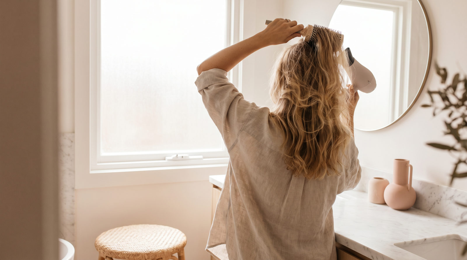 Mujer haciéndose un brushing en casa con cepillo redondo y secador