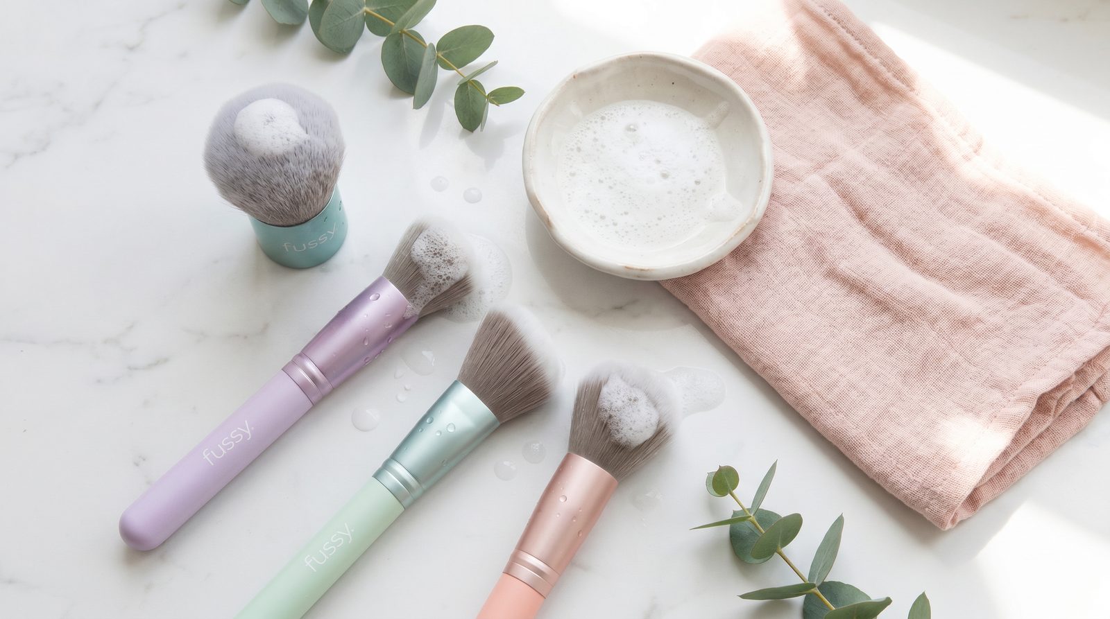 Brochas de maquillaje Fussy limpiándose con espuma sobre mármol