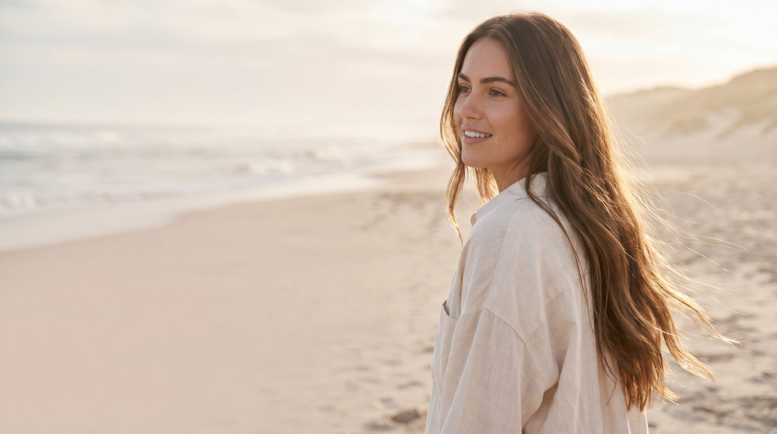 Mujer con el pelo sano y protegido en la playa al atardecer
